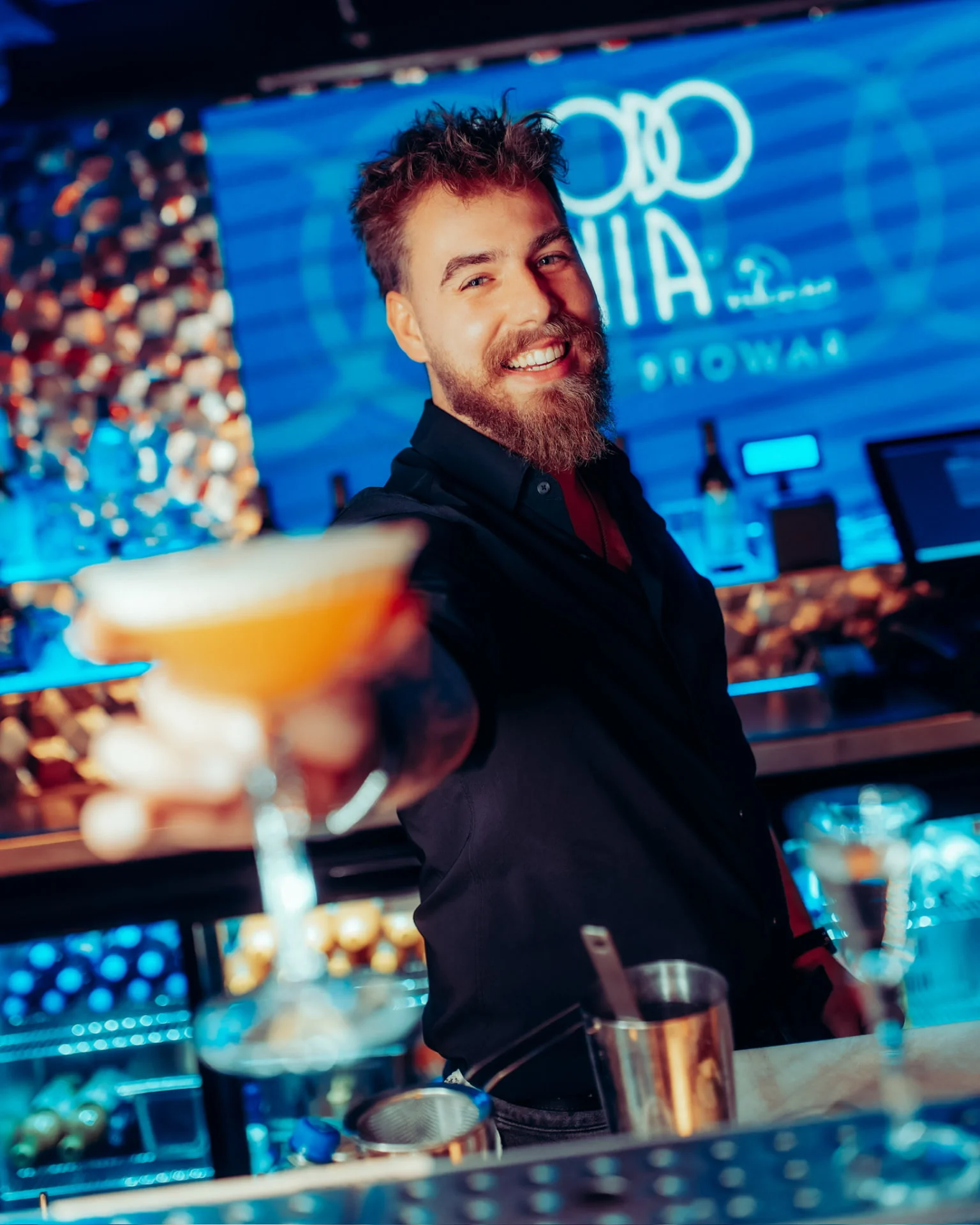 Barman podaje koktajl na tle niebieskiego baru