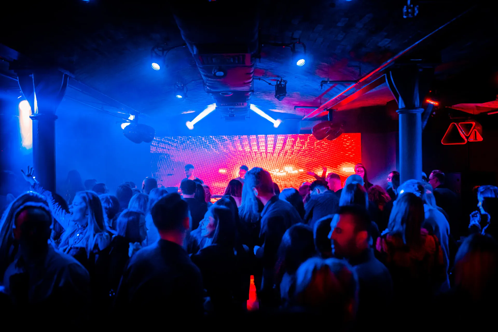 DJ-e za konsolą na tle czerwonego ekranu