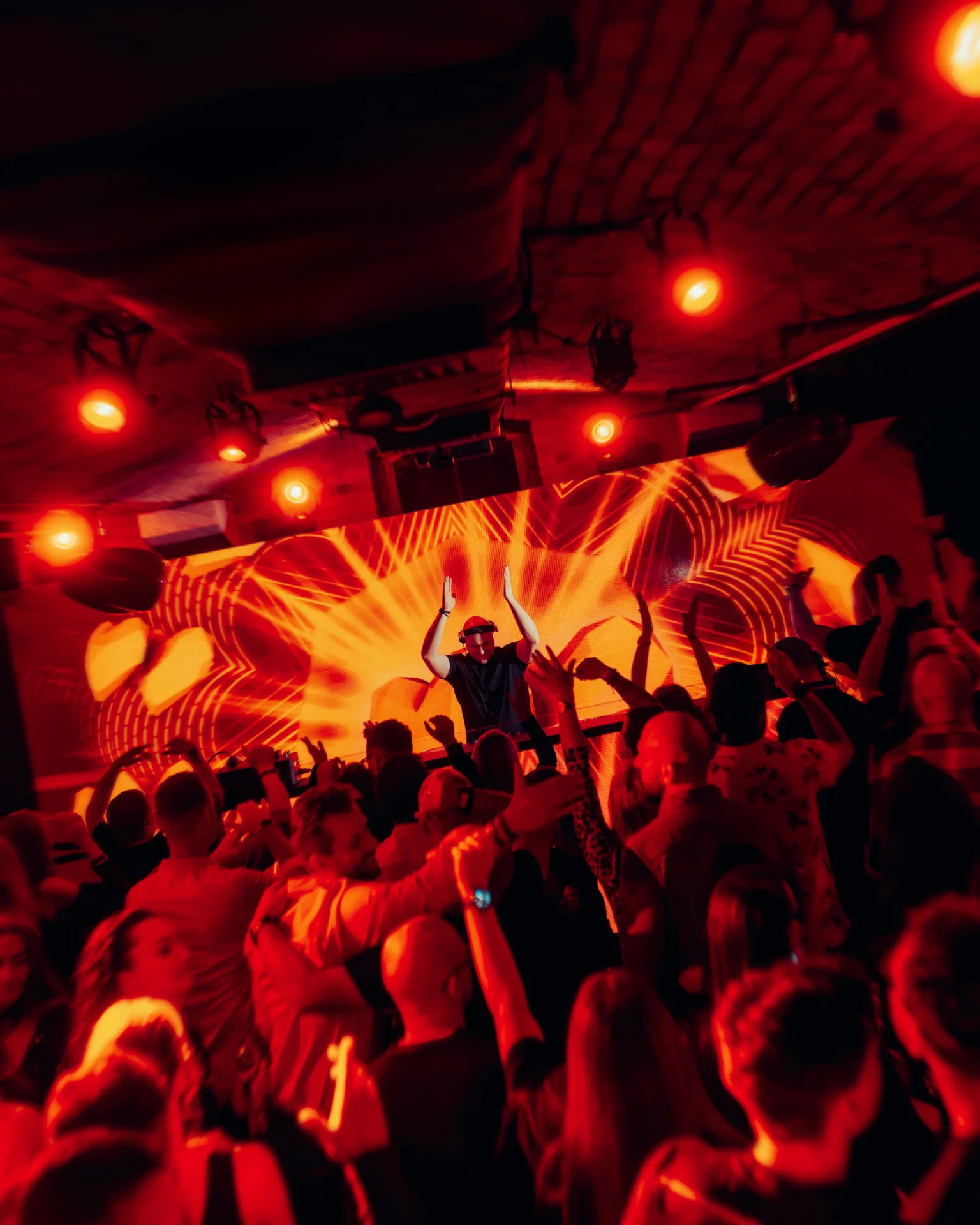DJ z uniesionymi rękami na tle pomarańczowego ekranu